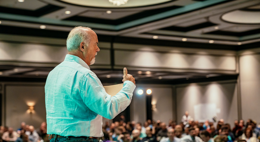man on stage talking to a crowd at a conference