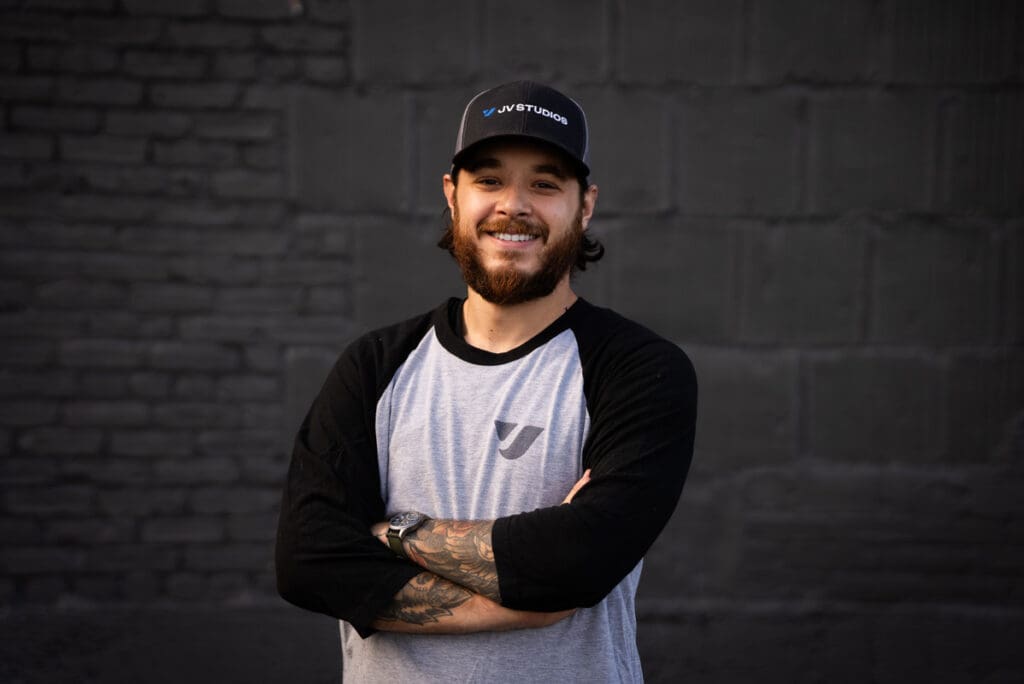 Male video producer wearing jv studios hat with arm crossed and tattoos