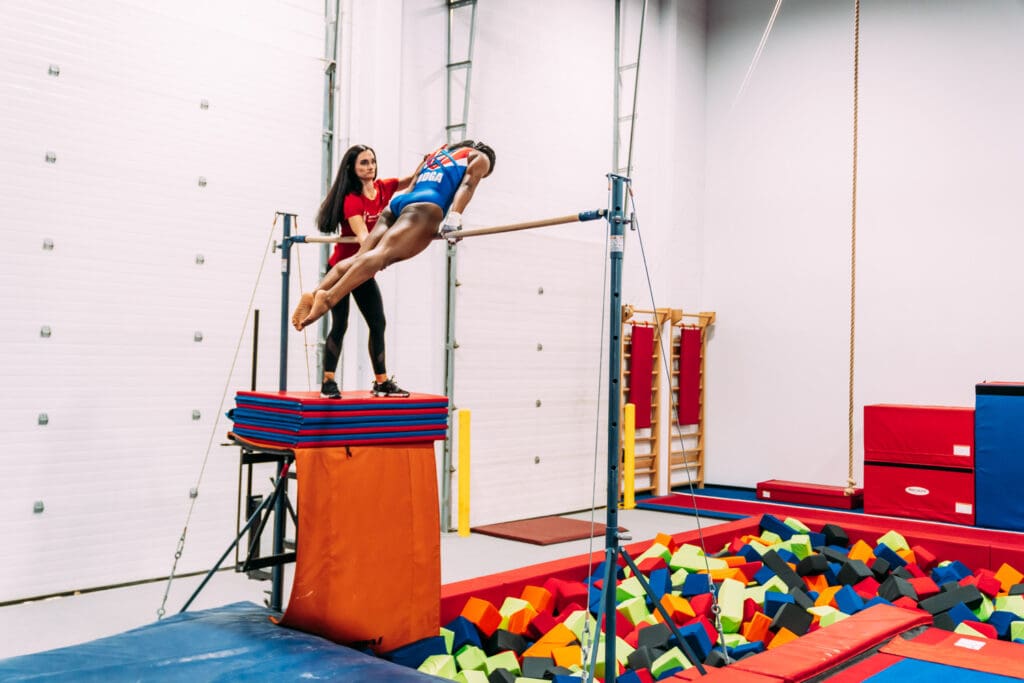 Gymnast on high bar with spotter