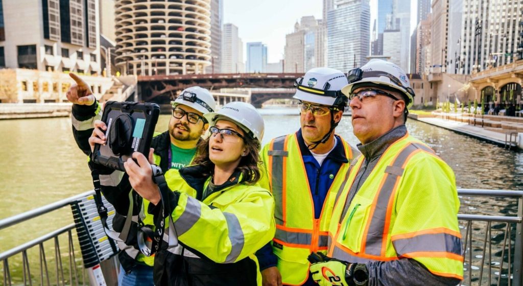 4 people in hard hats and vests looking up at a building