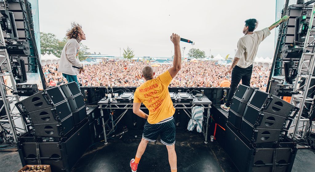 back of dj on stage looking at the crowd at a music festival